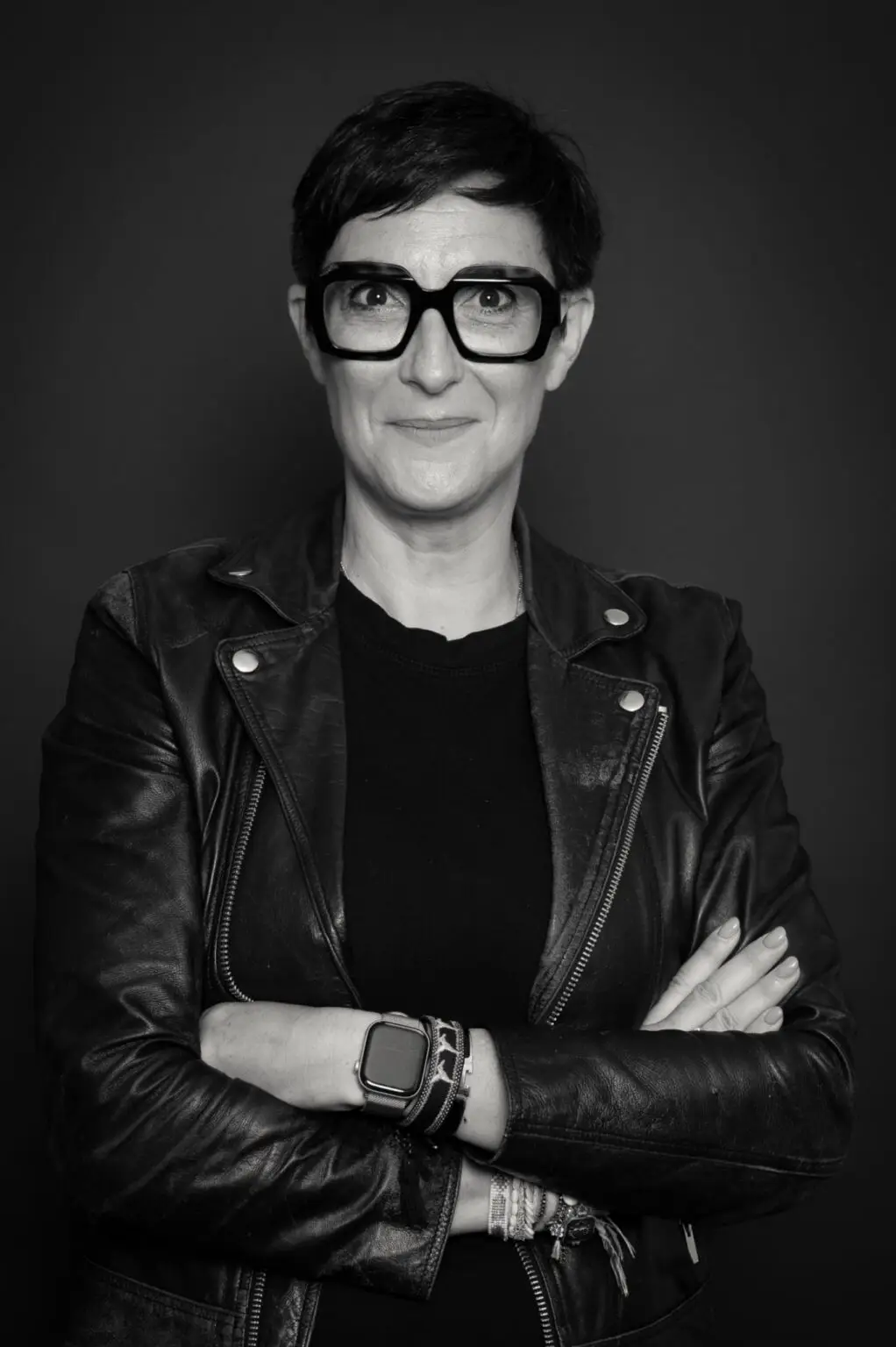 Portrait d'une experte en financement d'entreprise, femme aux lunettes et veste en cuir, les bras croisés, symbolisant la stratégie gagnante de diversification des partenaires bancaires.