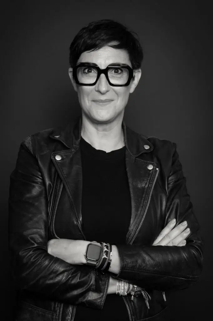 Portrait d'une experte en financement d'entreprise, femme aux lunettes et veste en cuir, les bras croisés, symbolisant la stratégie gagnante de diversification des partenaires bancaires.